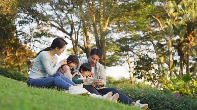 asian family with two children sitting on grass relaxing outdoors in city park