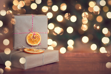 Christmas gift wrapped in a brown craft paper and decorated with slice of orange on a wooden background with copy space for text. Bokeh on the background