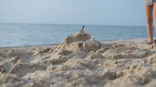 A boy tramples a sand castle on the seashore with his feet