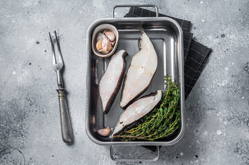 Fresh steak of raw fish halibut in kitchen tray with herbs. Gray background. Top view - obrazy, fototapety, plakaty