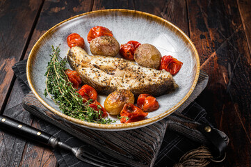 Grilled halibut fish steaks with tomato and potato in plate. Wooden background. Top view