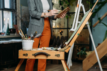 Painter working in real studio with oil paints and brushes, creating canvas, modern art. Young woman over window, closeup