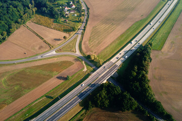 Highway crossroad with moving cars and trucks, aerial view. Asphalt road through countryside landscape