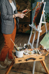 Painter working in real studio with oil paints and brushes, creating canvas, modern art. Young woman over window, closeup