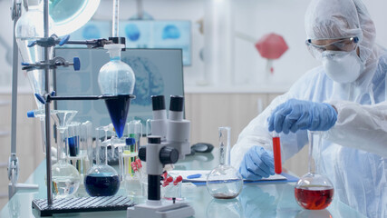 Fototapeta premium Scientist microbiologist doctor working with transparent glassware during biochemistry experiment in laboratory. Doctor man with ppe equipment mixing medical solution developing covid19 vaccine