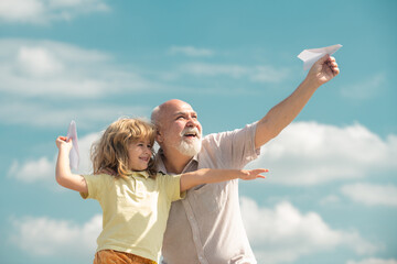 Child boy and grandfather with toy paper plane against summer sky background. Boy with dreams of flying. - obrazy, fototapety, plakaty