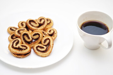 selective focus, Cinnamon sugar palmiers on white plate, blurred a cup of hot coffee
