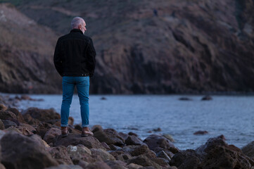 Adult man in black jacket standing on rocky beach looking at sea. Almeria, Spain