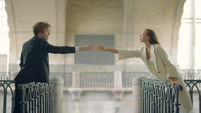 Lovers hold out their hands to each other at distance. Action. Beautiful couple in love on different sides of bridge reaches out to each other. Lovers stretch out their hands to each other over abyss