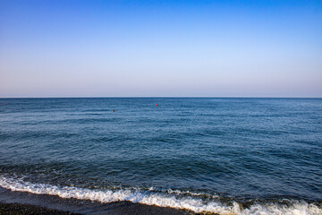 Morning with the calming waves of the Black Sea. On a warm sunny morning with blue cloudless skies. The coast of Sochi, Loo, Russia. - obrazy, fototapety, plakaty