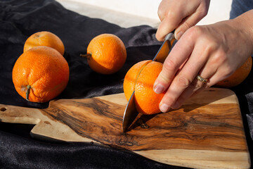 photo of the orange slicing process. A woman cuts an orange  with a knife on a wooden board