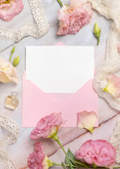 Pink flowers and a blank card with envelope laying on a marble table