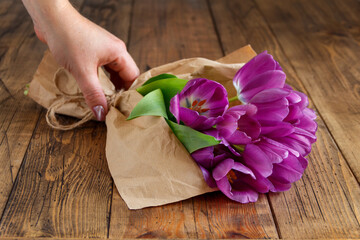 Hand with purple tulips bouquet in craft paper on wooden table