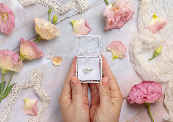 Woman hands holding a gift box with a pearl ring with light pink flowers around