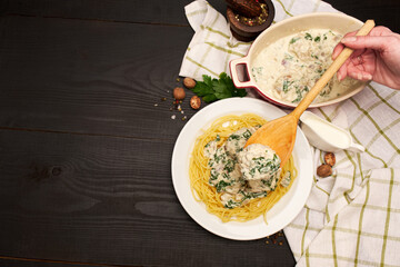 Portion of delicious meatballs with spinach in a creamy sauce and pasta on wooden background