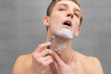 Close-up man shaving face, man's morning hygiene in bathroom, foam on face, shaving product concept