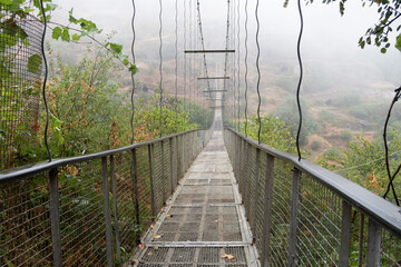 Fog view on the Khndzoresk suspension bridge in the cave city in the mountain rocks. Armenia landscape attraction. Abandoned ruins in the mist. Atmospheric stock photo.