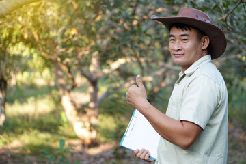 Asian male botanist holds paper clipboard and thumbs up, stands at forest. Concept : Survey and research botanical plants. Forest conservation.