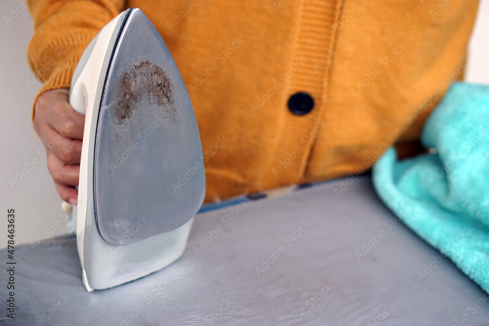 Wall mural a housewife holds dirty iron with burnt stain on iron surface. concept : damage on appliance from wo