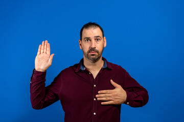 Young handsome man wearing casual shirt standing over isolated blue background. Swearing with hand on chest and open palm, making a loyalty promise oath