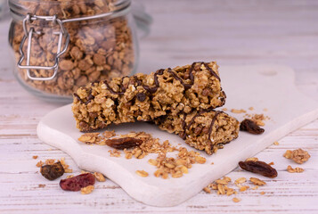 Granola bars with nuts and raisins and pieces of chocolate on a white wooden board.