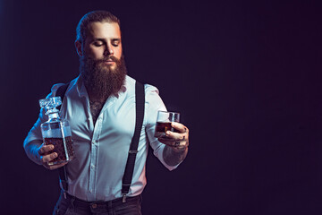 Brutal bearded man holds whiskey in his hands, dressed in white shirt. Studio shot