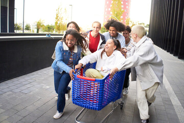 Crazy friends making a racing challenge with shopping cart. Multiracial group of young people...