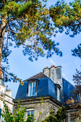 A beautiful old house in Jardin des Plantes, in Paris with chimney and blue roof from a view between tree branches 