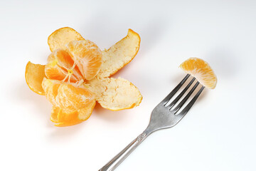 Disconnected from peel tangerine with juicy slices and fork, on a white background