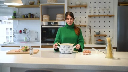 Young vlogger woman vlogging about cooking at her apartment domestic kitchen cook and making video vlog with smartphone as online content creator for internet. Female influencer making a meal.