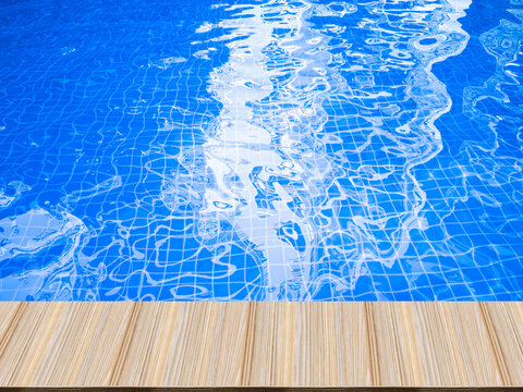 Artificial wooden tables in front, blue water waves in the swimming pool, and hotel reflections.