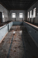 An old abandoned swimming pool. Wooden chair at the bottom. Dirty floor. Shabby walls. Blue tiles. An old abandoned building.