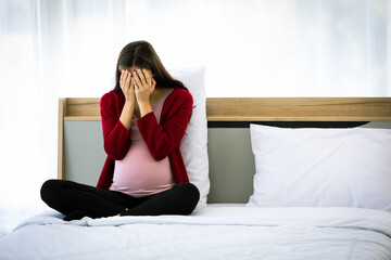 Caucasian millennial young stressed depressed upset worried unhappy lonely female prenatal pregnant mother in casual pregnancy outfit sitting holding hands cover face crying alone on bed in bedroom