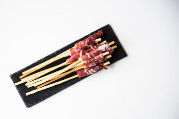 Slices of acorn-fed Iberian ham with breadsticks, Spanish tapa, for events, dinners or celebrations, on a black slate