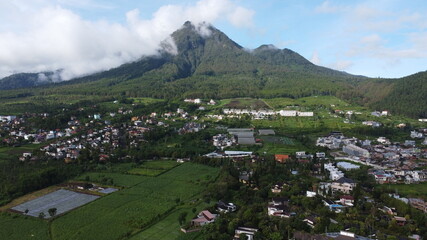 Fototapeta na wymiar Drone photo of mountain view in Batu City, Indonesia surrounded with white clouds and small buildings
