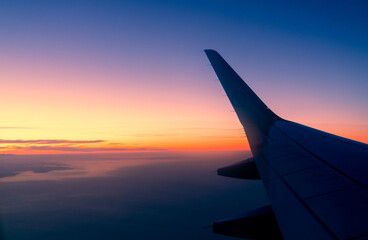 Wing of plane with sunrise skyline. Airplane flying in the sky. Scenic view from airplane window....