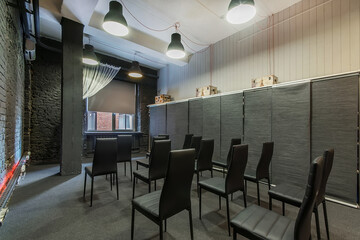 A spacious loft room with gray-black brick walls, a window and rows of chairs for presentations.