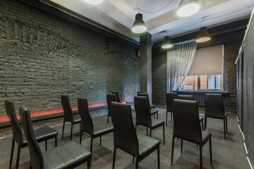 An open loft space with dark gray brick walls. a window and rows of coworking chairs.