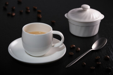White cup of coffee on a black textured table. Cup of coffee on a black background. Coffee beans on black slate. Breakfast coffee on a black background.
