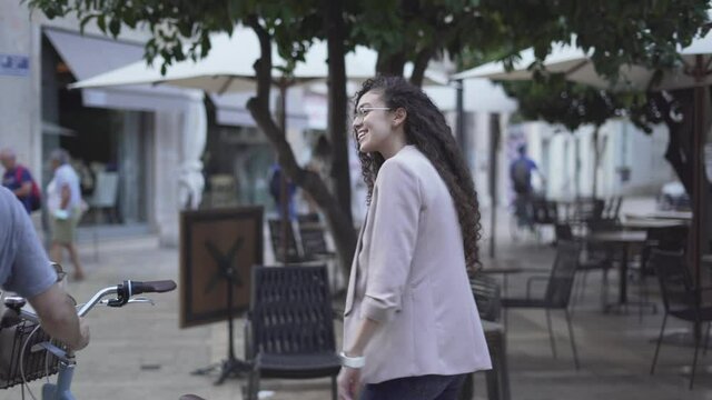 Moroccan Girl In Coat And Curly Long Hair Walking In The Street Together With A Man Pushing A Bike. - tracking shot