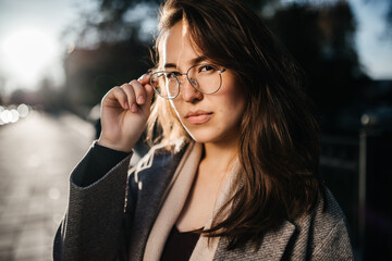 a beautiful girl looks into the camera and adjusts her glasses