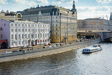 Moscow, Russia - June 16, 2019: Pleasure boat sails along Moscow River in direction of Stalin's skyscraper on Kotelnicheskaya Embankment. View of Hotel Baltschug Kempinski on Raushskaya Embankment.