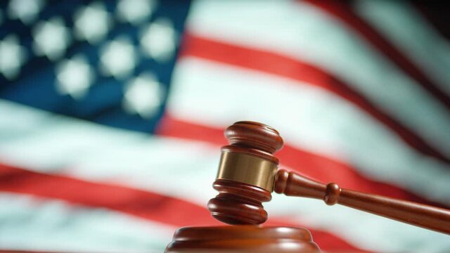 A judge gavel with a flag of United States of America on background. Close up of wooden hammer and legal lawyer books or codex. Sentence law or legal system and jurisprudence or court concept.