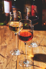 Red, white and rose wine in glasses on wooden background and collection of wine bottles, copy space