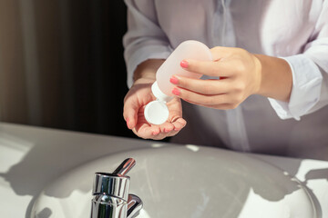 Woman applying cream after washing hands for protective and care dry skin near white sink in bathroom with sunlight from the window.