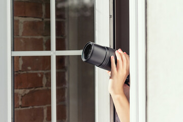 Private detective with spying zoom lens camera taking picture through open window. Close – up. concept
