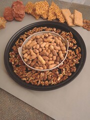 Bowl of groundnuts or peanuts with a black tray of walnuts with folk punjabi winter sweet dishes in the background for lohri festival. 