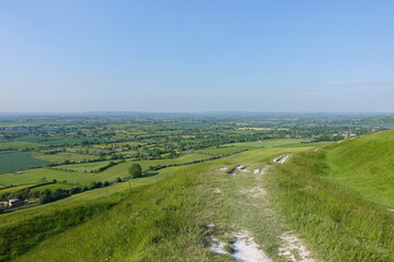 Scenic view of a elevated landscape with a footpath, green fields and blue sky above