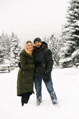 Fototapeta na wymiar Attractive man and woman cuddling in the frosty forest. Adult couple in puffer jacket have fun on walk. Romantic date in winter time.Winter lovestory