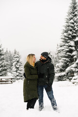 Attractive man and woman cuddling in the frosty forest. Adult couple in puffer jacket have fun on walk. Romantic date in winter time.Winter lovestory